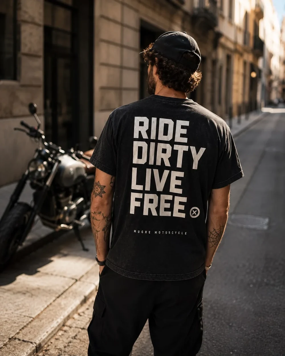 Rider con la camiseta NOMAD de espaldas, junto a su moto en una calle de Barcelona